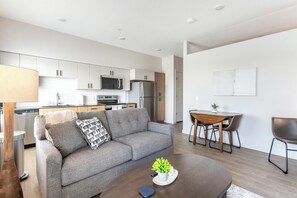 Una sala de estar moderna con un sofá gris, una mesa de centro con una planta, y un comedor con una mesa y sillas de madera.