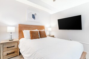 Une chambre d’hôtel avec un grand lit, deux tables de chevet avec des lampes, un téléviseur à écran plat fixé au mur et une œuvre d’art décorative au-dessus du lit.