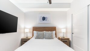 A hotel room with a large bed, two bedside tables with lamps, a flat-screen TV mounted on the wall, and a door to the right. - Landing | Stunning Studio, Courtyard, Pool (Salt Lake City)