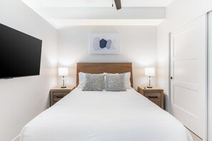 A hotel room with a large bed, two bedside tables with lamps, a flat-screen TV mounted on the wall, and a door to the right. - Landing | Stunning Studio, Courtyard, Pool (Salt Lake City)