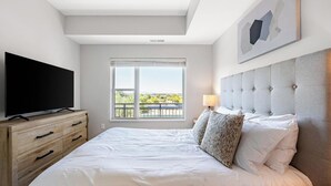 Ein Hotelzimmer mit einem großen Bett, einem Flachbildfernseher, einer Holzkommode, einem Fenster mit Aussicht und einer Deckenleuchte.