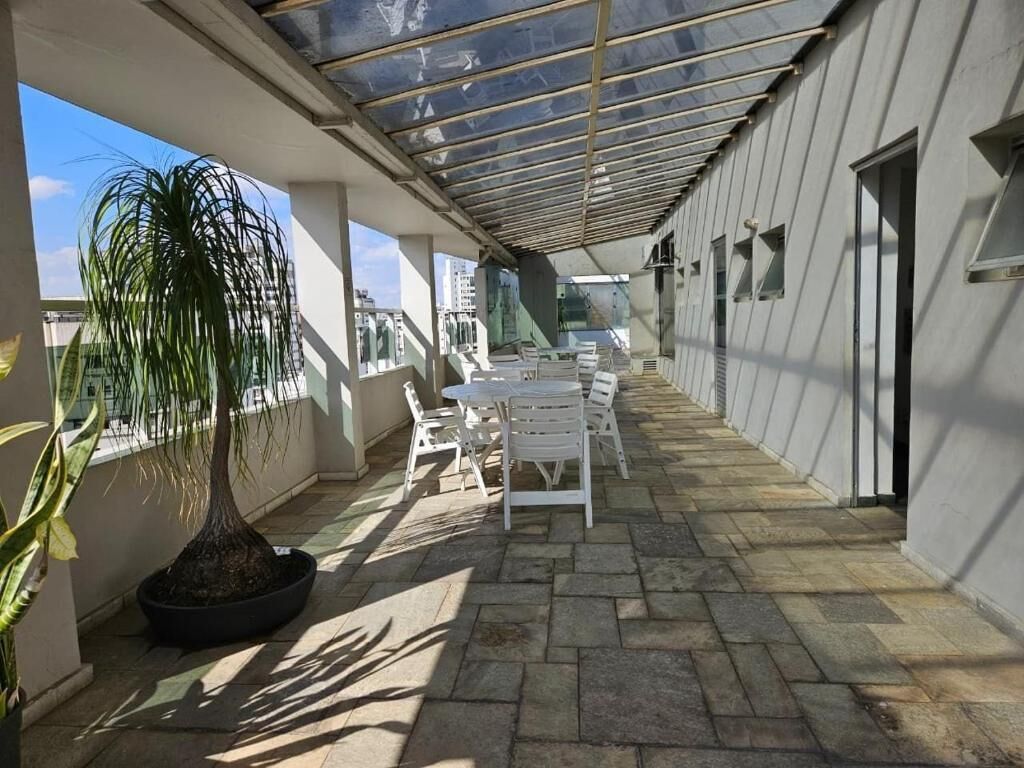Uma área externa coberta com mesa e cadeiras, uma planta em vaso e vista para edifícios.