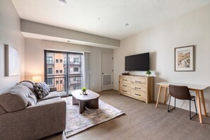 A modern living room with a sofa, coffee table, TV, and a desk with a chair. - Landing | Modern 1BD, Yoga Studio, Game Room (Salt Lake City)