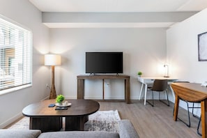 A modern living room with a flat-screen TV, a wooden coffee table, a sofa, a desk with a chair, and a lamp. - Landing | Spectacular Studio, Pool, Gym (Salt Lake City)