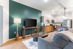A modern living room with a flat-screen TV, a wooden side table, and a sofa. - Landing | Amazing 1BD, Game Room, Yoga Studio (Salt Lake City)