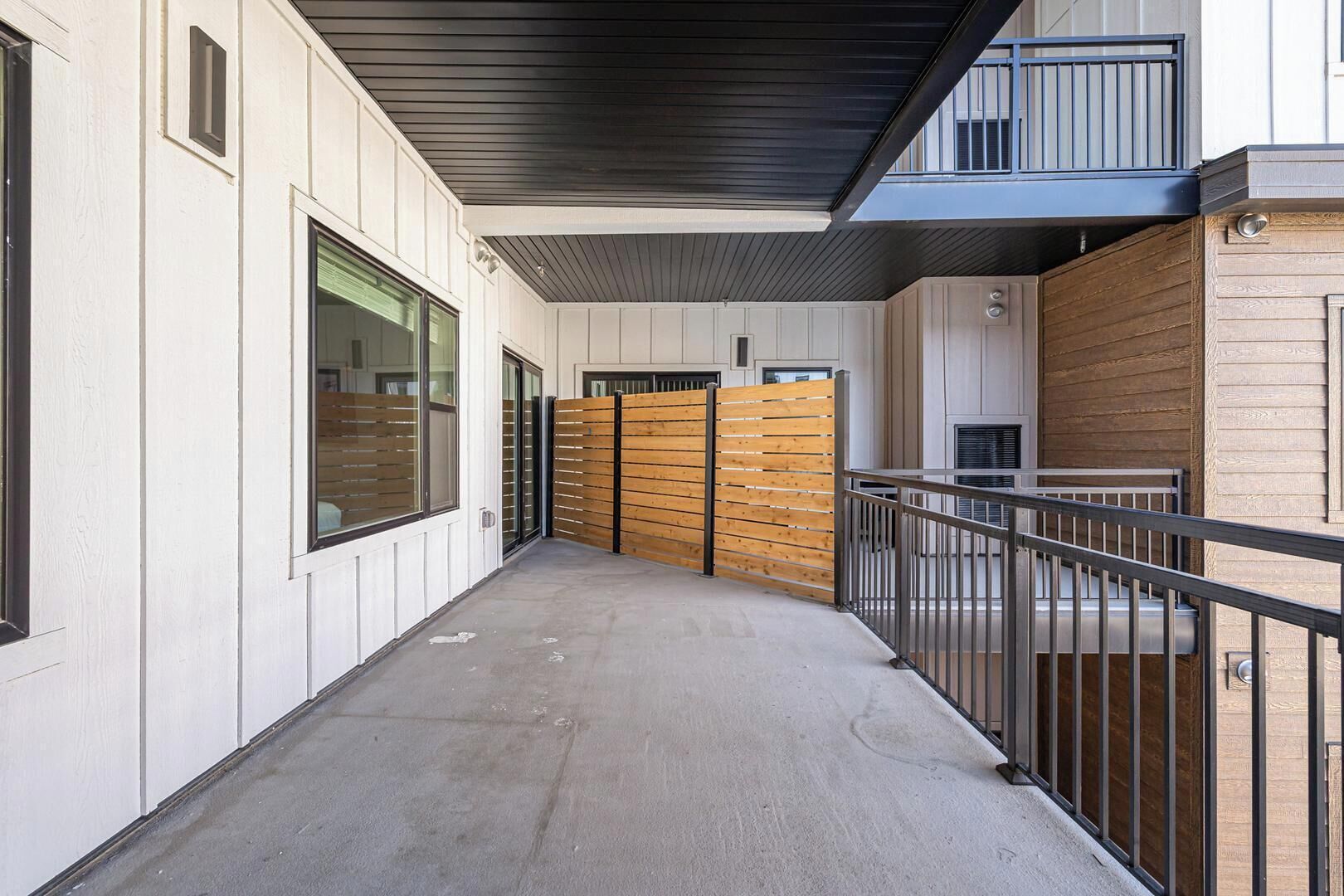 Un couloir avec une porte en bois, un sol en béton et une rambarde en métal.