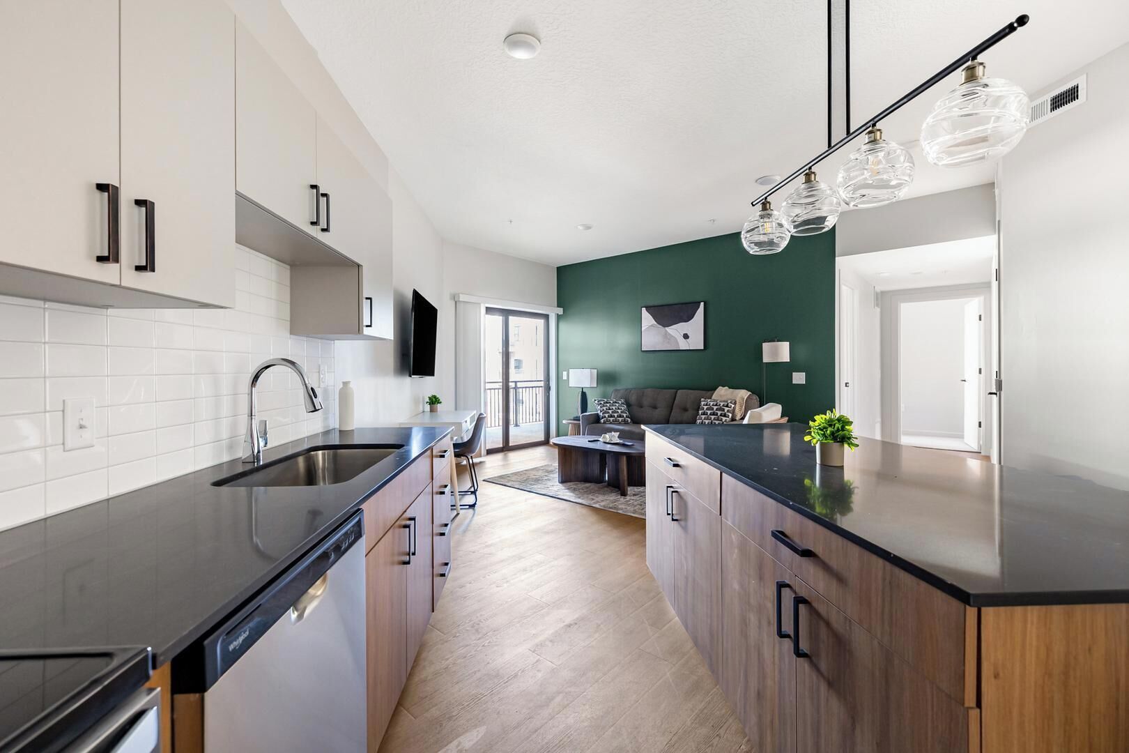 Une cuisine moderne avec un îlot central, un coin repas doté d’un canapé et un mur d’accent de couleur verte.