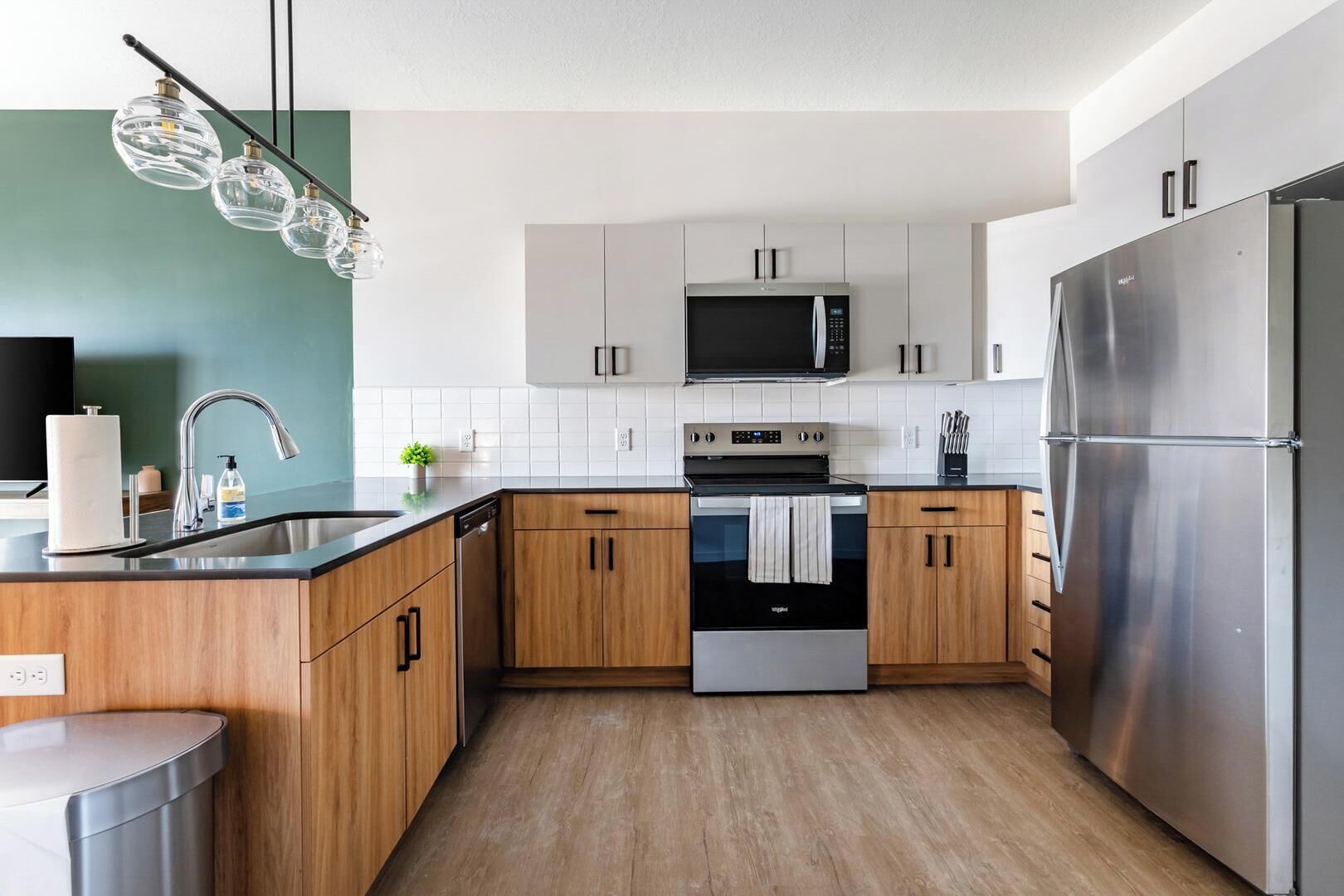 A modern kitchen with stainless steel appliances, wooden cabinets, and a black countertop.