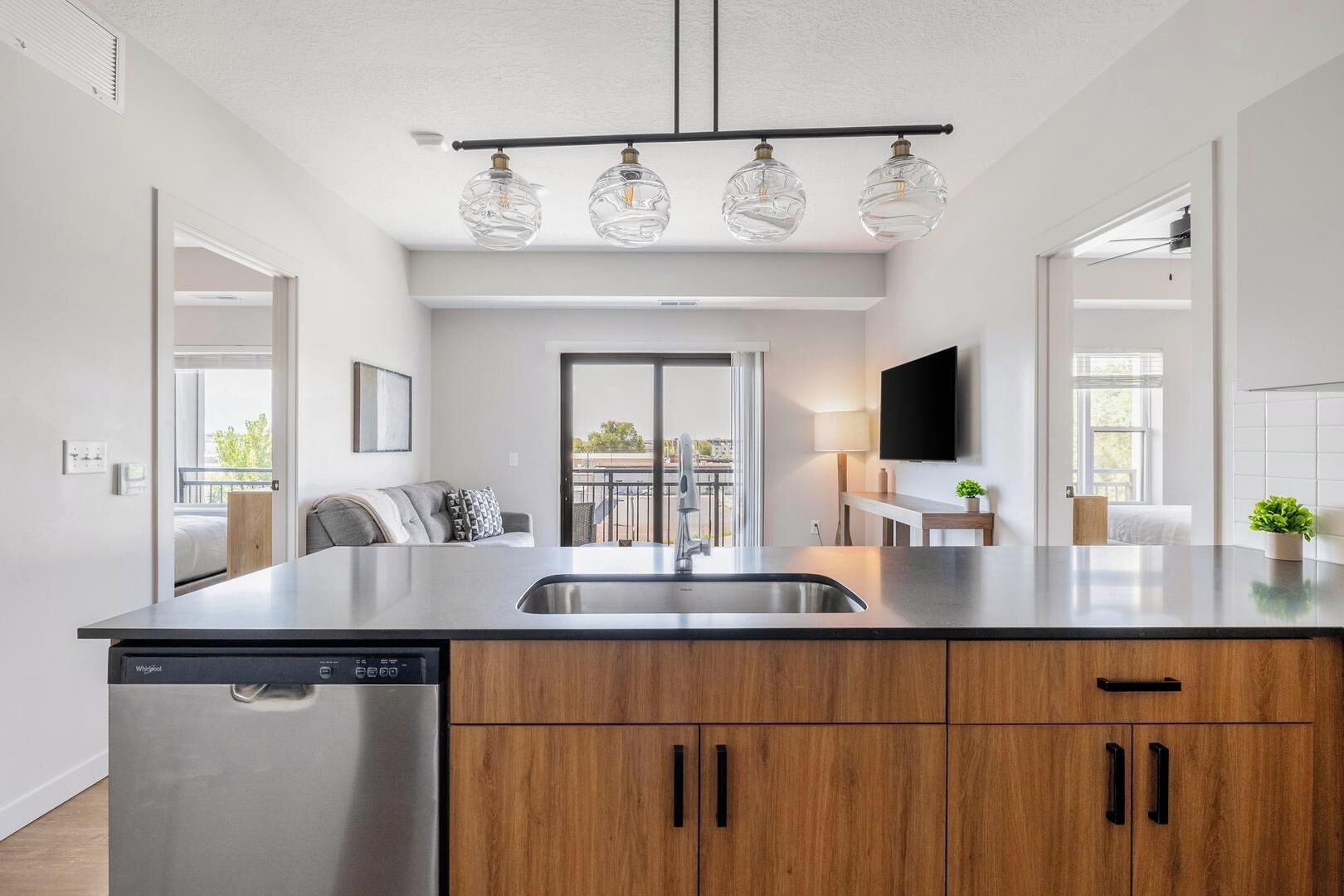 A modern kitchen with a stainless steel dishwasher, wooden cabinets, a central island with a sink, and a ceiling-mounted light fixture.