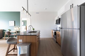 A modern kitchen with a stainless steel refrigerator, wooden cabinets, and a black countertop. - Landing | Incredible 2BD, Game Room, Courtyard (Salt Lake City)