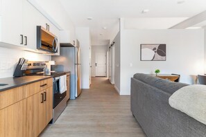Eine moderne Küche mit Holzschränken, Edelstahlgeräten und einem grauen Sofa in einem Flur.
