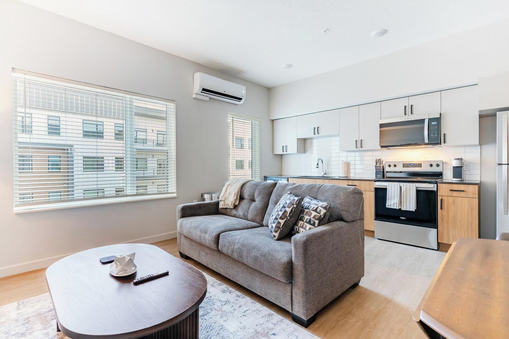 A modern apartment with a grey sofa, a dining table, and a kitchen area.