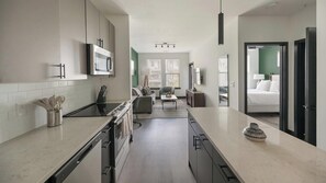 Eine moderne Küche mit einer Kochinsel, ein Essbereich mit Sofa und Tisch, sowie ein Schlafzimmer mit Bett und Nachttisch.