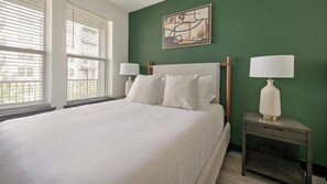A hotel room with a large bed, two bedside tables with lamps, a green accent wall, and a window with blinds. - Landing | Stylish 1BD (Nashville)
