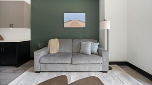 Un salon moderne avec un canapé gris, une petite plante en pot et un tableau encadré accroché au mur.