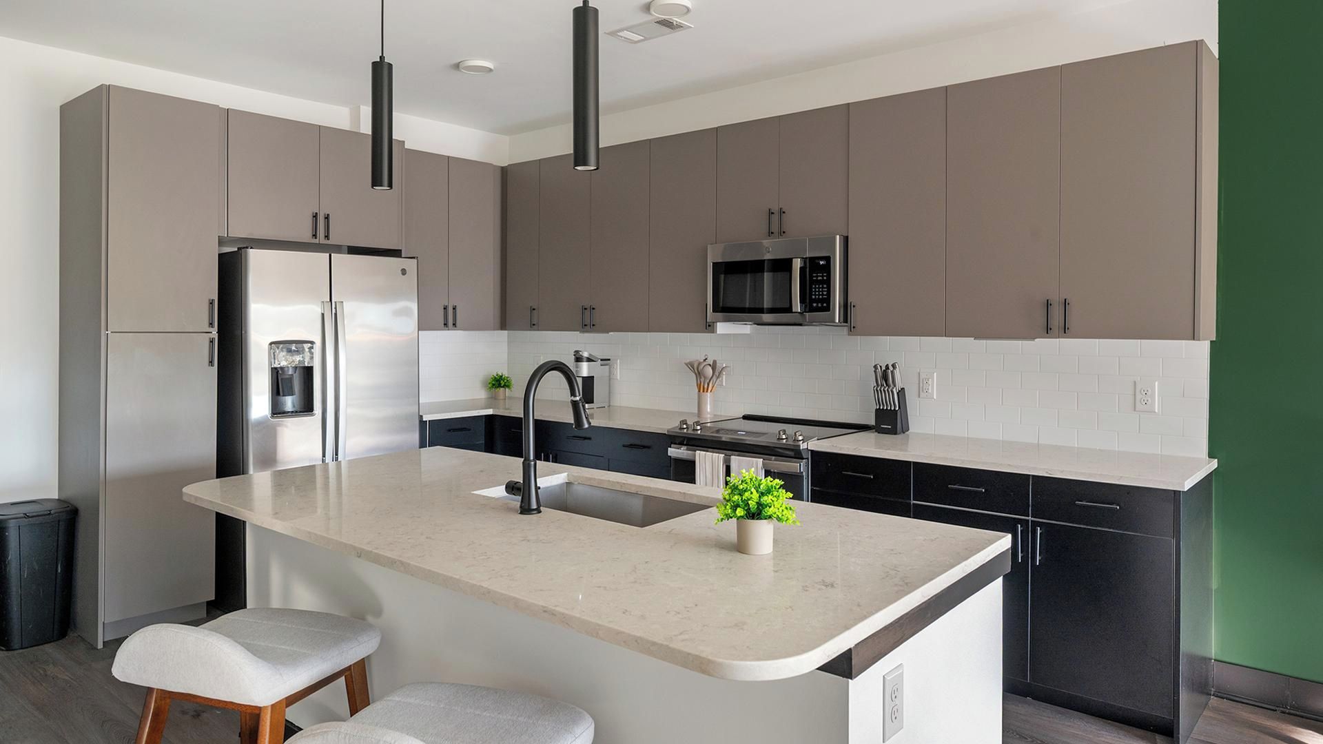 Une cuisine moderne dotée d’un îlot central, d’appareils électroménagers en acier inoxydable et d’un mur d’accent vert.