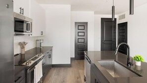 Cozinha moderna com eletrodomésticos de aço inoxidável, bancada preta e piso de madeira.