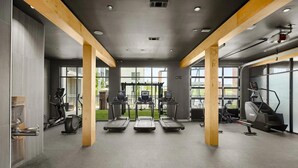 Una palestra con tapis roulant, ellittiche e una cyclette, caratterizzata da ampie finestre e travi in legno.