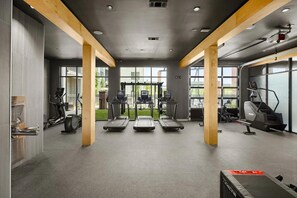 Ein Fitnessstudio mit Laufbändern, Crosstrainern und einem Ergometer, ausgestattet mit großen Fenstern und Holzbalken.