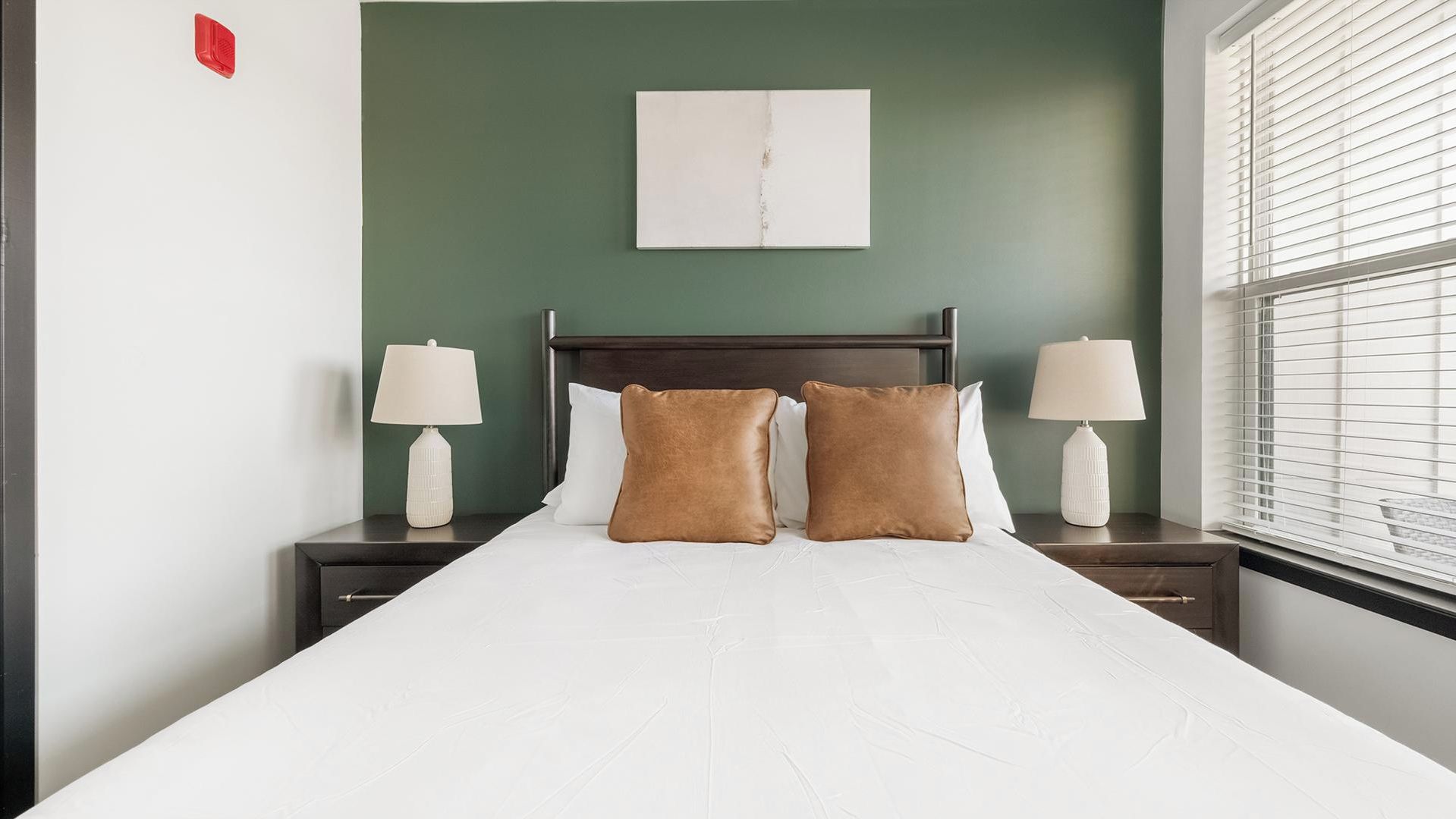 A hotel room with a bed, two nightstands, two lamps, a headboard, and a window with blinds.
