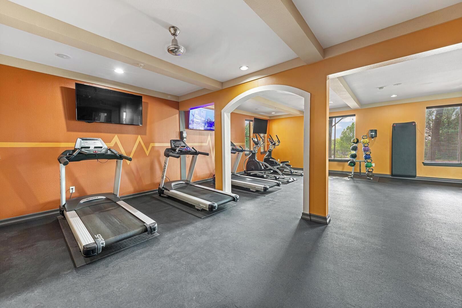 A gym with treadmills, a TV, and a wall-mounted screen.