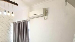 A bedroom with a bed, a window with curtains, an air conditioning unit, and a wooden floor. - Abrisam Shareeah Family Homestay (Yogyakarta)
