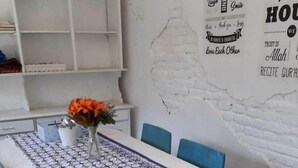 A dining area with a table covered by a patterned tablecloth, blue chairs, and a vase with orange flowers. - Abrisam Shareeah Family Homestay (Yogyakarta)