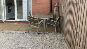 Un patio con una mesa redonda y cuatro sillas, una cerca de madera y un muro de ladrillo.