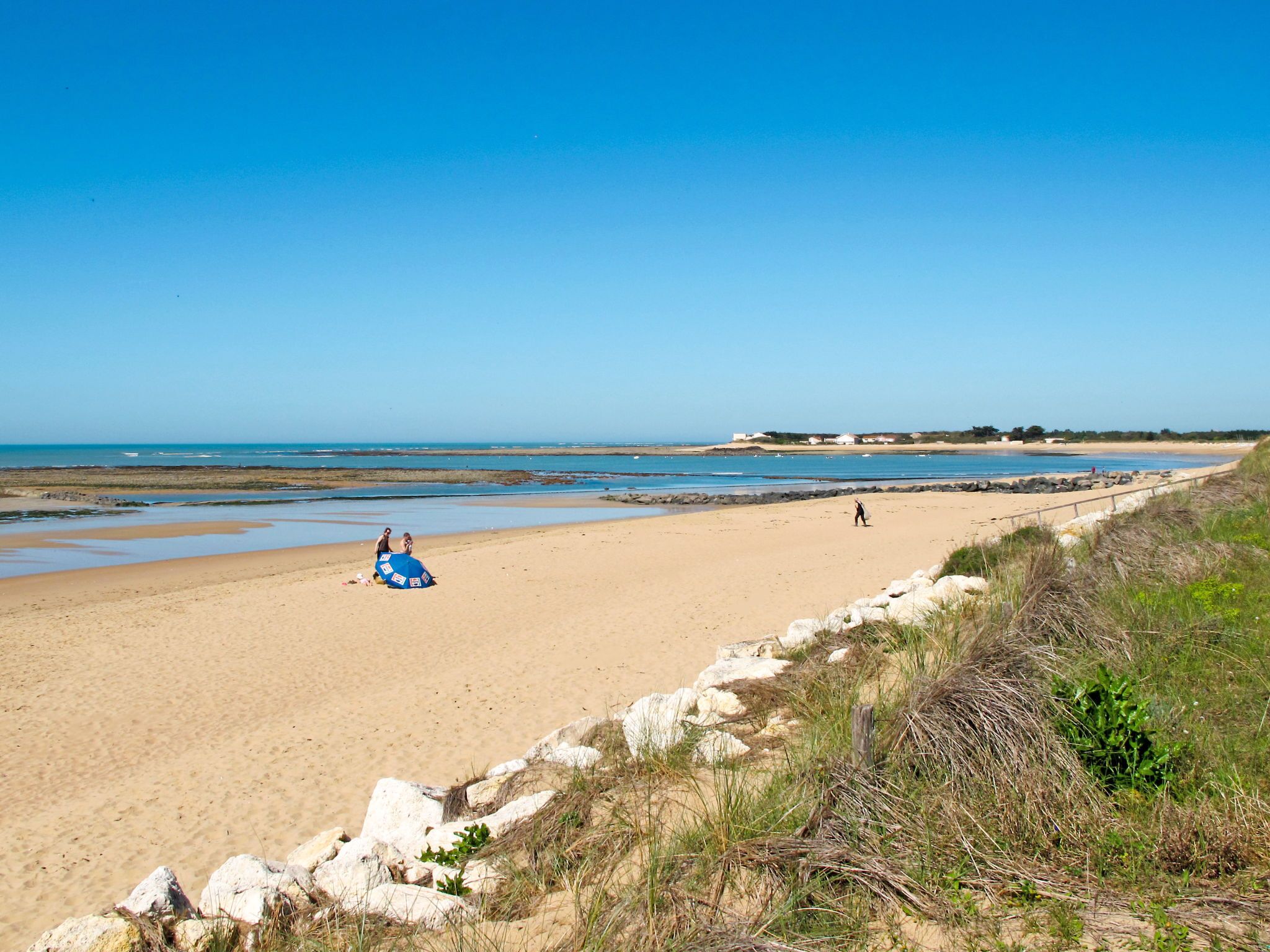 Een strand met een zandige kust, een rotsenrij en een helderblauwe lucht.