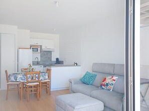 A modern apartment with a dining area, kitchenette, grey sofa with patterned cushions, and a glass door leading to an outdoor area. - Coeur d'Oléron by Interhome (Ile d'Oléron)