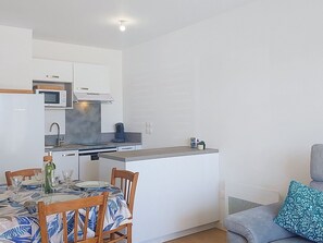 A compact kitchen with a microwave, stove, and sink. There is a dining table with chairs and a small sofa with a patterned cushion. - Coeur d'Oléron by Interhome (Ile d'Oléron)