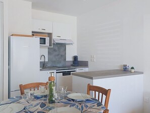 A compact kitchen with a refrigerator, microwave, and coffee maker. There is a dining table with chairs and a patterned tablecloth. - Coeur d'Oléron by Interhome (Ile d'Oléron)