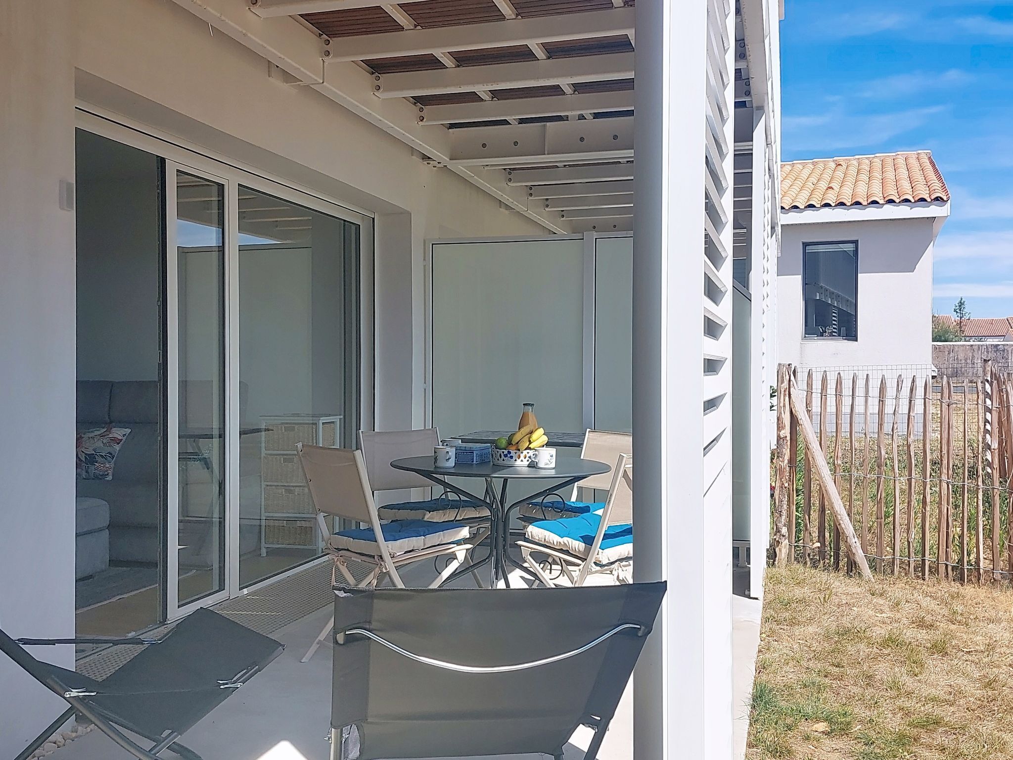Een overdekt terras met een tafel, stoelen en een kleine tuin.