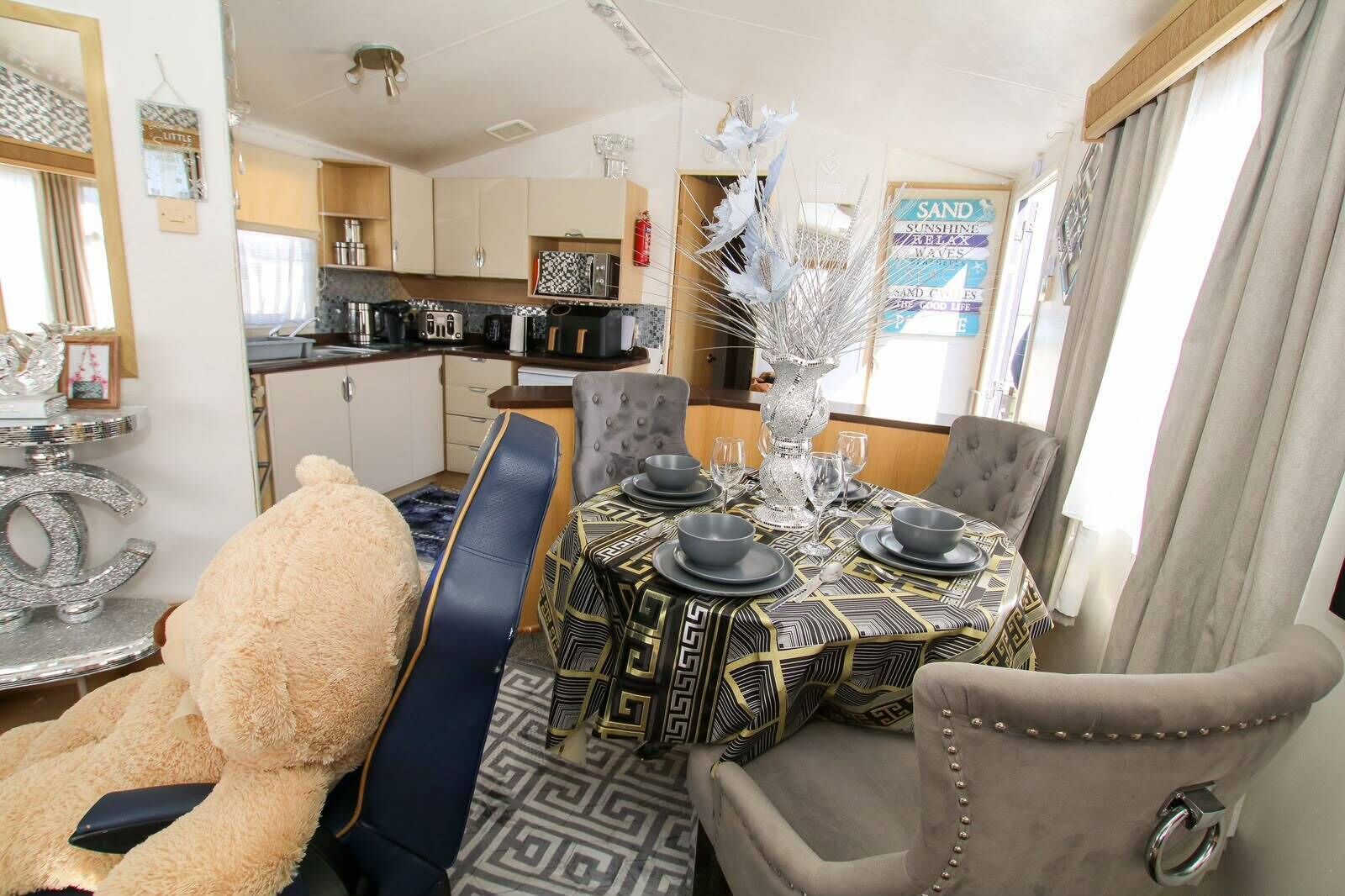 A dining area with a round table set for four, a plush chair, a decorative vase, and a kitchen in the background.