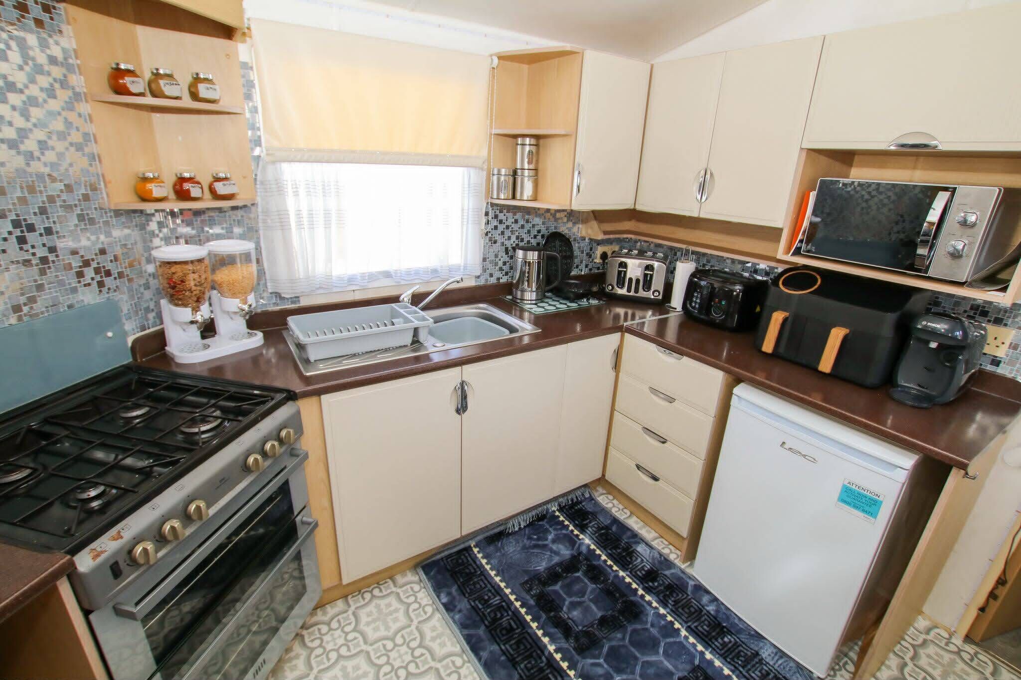 Una cocina compacta equipada con estufa a gas, horno, microondas, tostadora y un refrigerador pequeño.