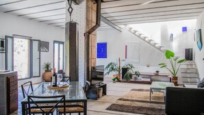 Uma sala de estar moderna com mesa de jantar de vidro, assentos confortáveis, escada e diversas plantas.