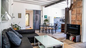Sala moderna com sofá, mesa de centro e televisão, conectada a uma cozinha com área de refeições.