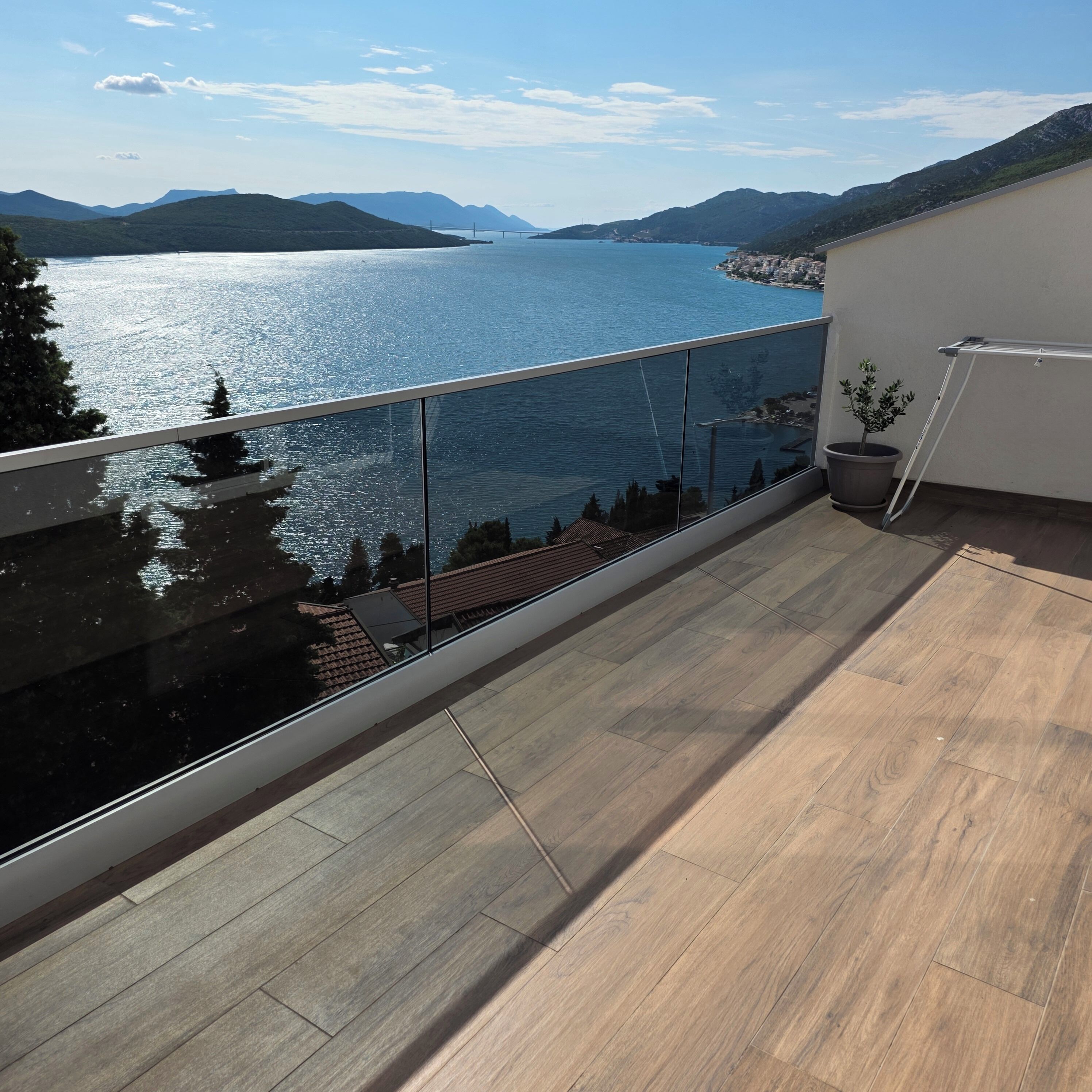 A balcony with a view of a lake and mountains, a potted plant, and a metal railing.