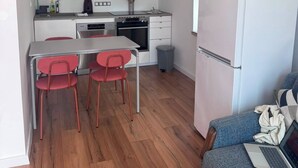 Uma cozinha compacta com armários brancos, uma mesa de jantar com cadeiras vermelhas, forno embutido e uma geladeira branca.