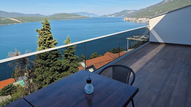 Uma varanda com vista para um lago e montanhas, uma mesa com uma garrafa e uma cadeira.