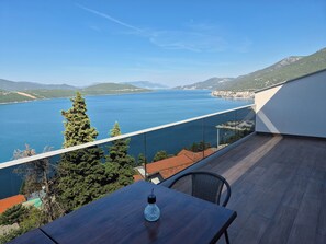 Uma varanda com vista para um lago e montanhas, uma mesa com uma garrafa e uma cadeira.
