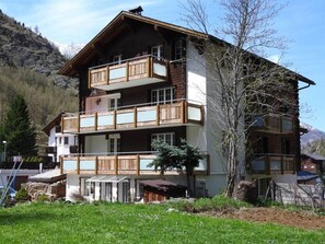Ein mehrgeschossiges Gebäude mit Balkonen, einer Holzfassade und einem Bergpanorama im Hintergrund.