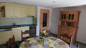 A compact kitchen with a dining area, featuring a table with a floral tablecloth, wooden chairs, and a cabinet with glass doors. - Alpenperle Appartement/Fewo 6-Bettwohnung by Interhome (Saas-Almagell)