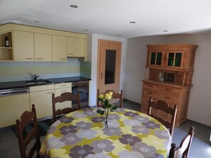A compact kitchen with a dining area, featuring a table with a floral tablecloth, wooden chairs, and a cabinet with glass doors. - Alpenperle Appartement/Fewo 6-Bettwohnung by Interhome (Saas-Almagell)