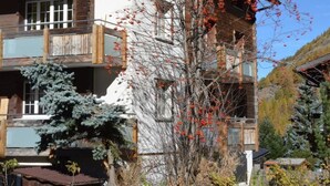 A multi-story wooden building with balconies, a tree with red leaves, and a clear blue sky. - Alpenperle Appartement/Fewo 6-Bettwohnung by Interhome (Saas-Almagell)