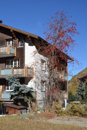 A multi-story wooden building with balconies, a tree with red leaves, and a clear blue sky. - Alpenperle Appartement/Fewo 6-Bettwohnung by Interhome (Saas-Almagell)