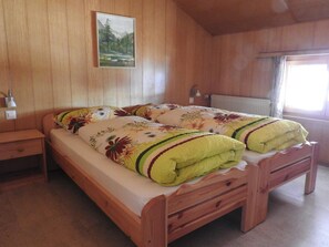 Ein hölzernes Bett mit floralem Überwurf und zwei Kissen, ein Nachttisch, eine Lampe und ein Fenster mit Vorhängen.