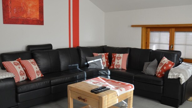 A living room with a black leather sectional sofa, a wooden coffee table, and red and white patterned pillows. - Alpenperle Appartement/Fewo 6-Bettwohnung by Interhome (Saas-Almagell)