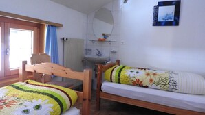 A bedroom with two wooden beds, a window with curtains, a sink, and a mirror on the wall. - Alpenperle Appartement/Fewo 6-Bettwohnung by Interhome (Saas-Almagell)