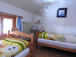 A bedroom with two wooden beds, a window with curtains, a sink, and a mirror on the wall. - Alpenperle Appartement/Fewo 6-Bettwohnung by Interhome (Saas-Almagell)